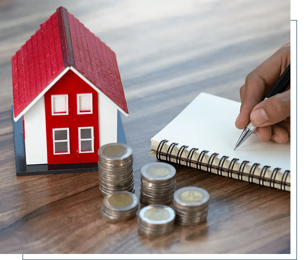 A hand writes in a notebook near a small red house and stacked coins.