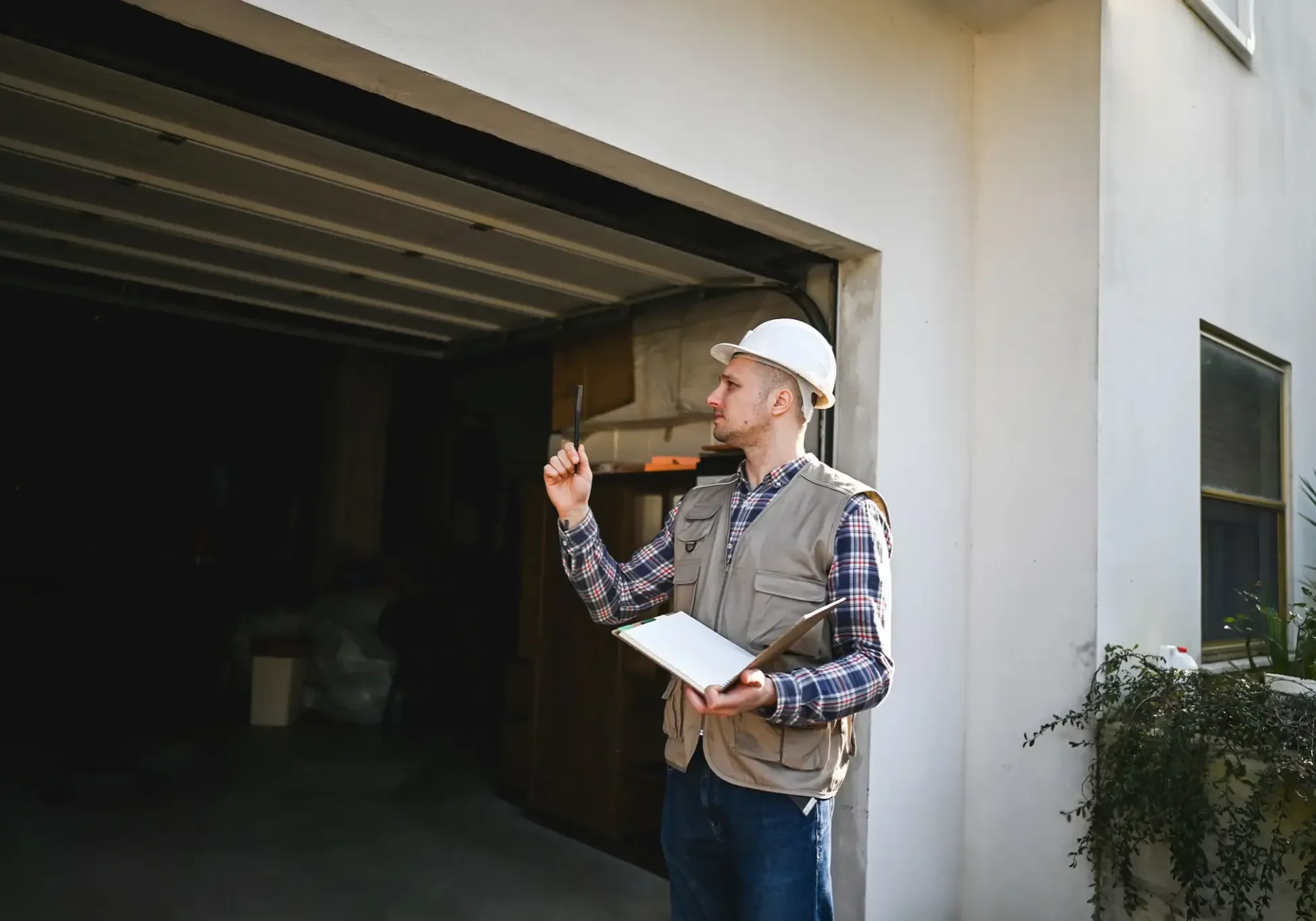 A construction worker inspecting a garage door while holding a clipboard.